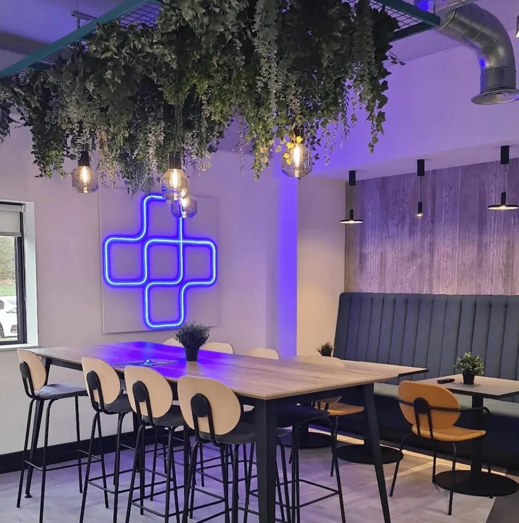 Modern restaurant interior with blue neon plus sign.